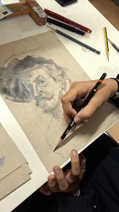 Mão de um aluno a desenhar um retrato a grafite