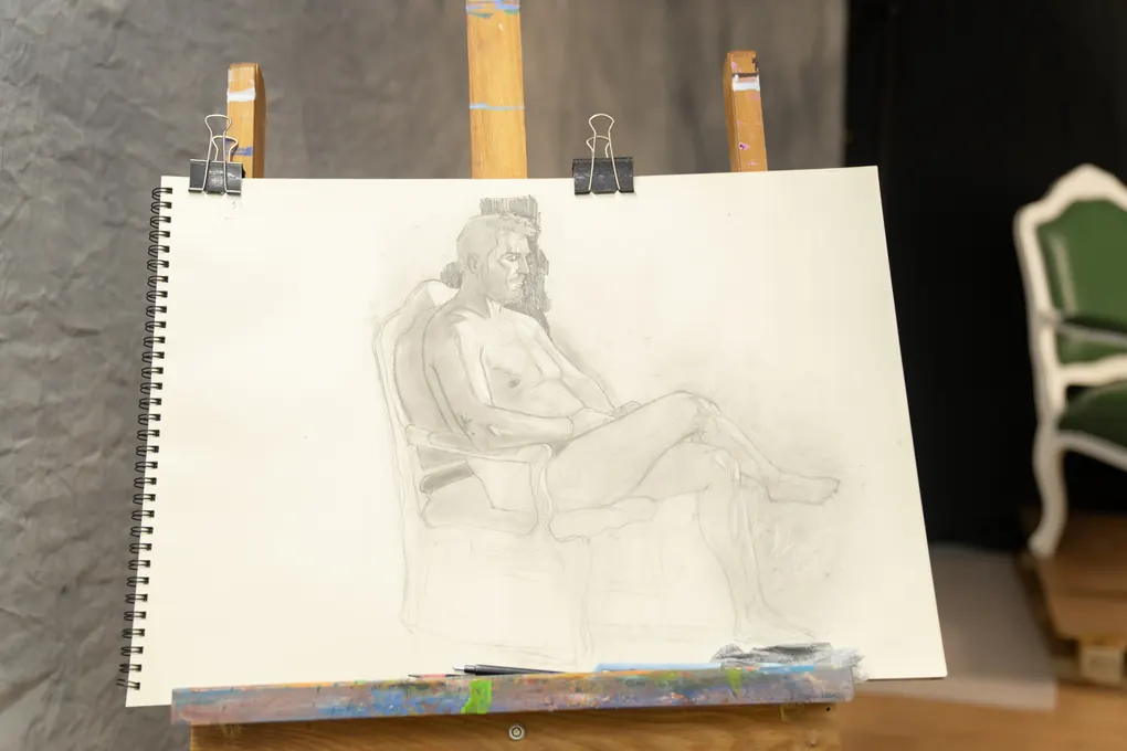 Figura sentada desenhada a grafite, presa ao cavalete